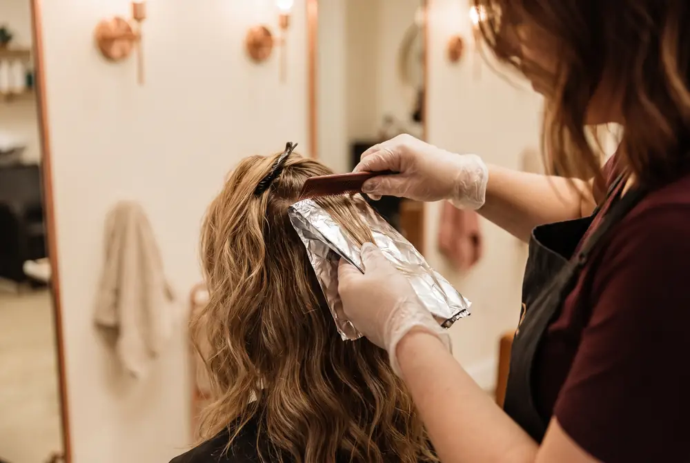 Manos de una peluquera colocando papel de aluminio para unas mechas en el pelo de una clienta